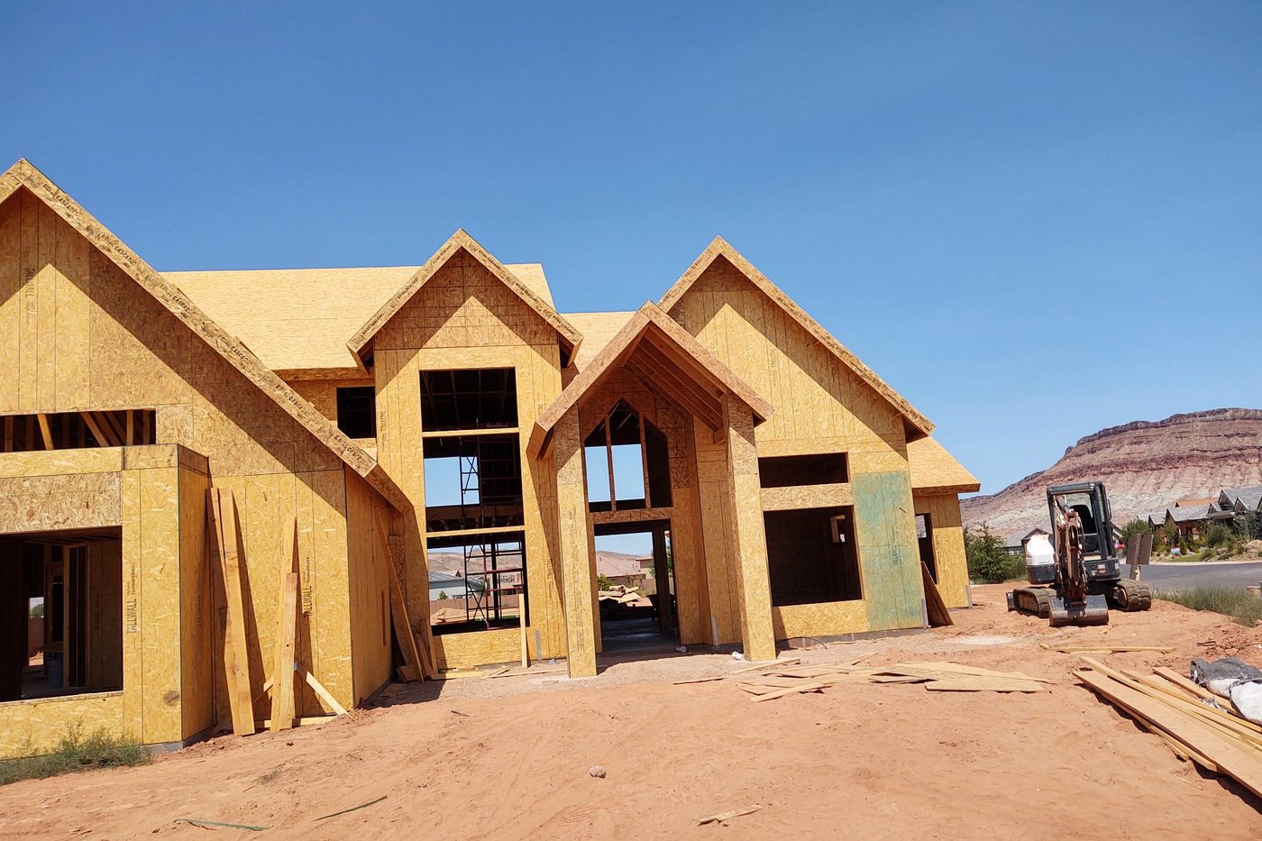 Framed and sheathed home with multiple gables under a blue sky
