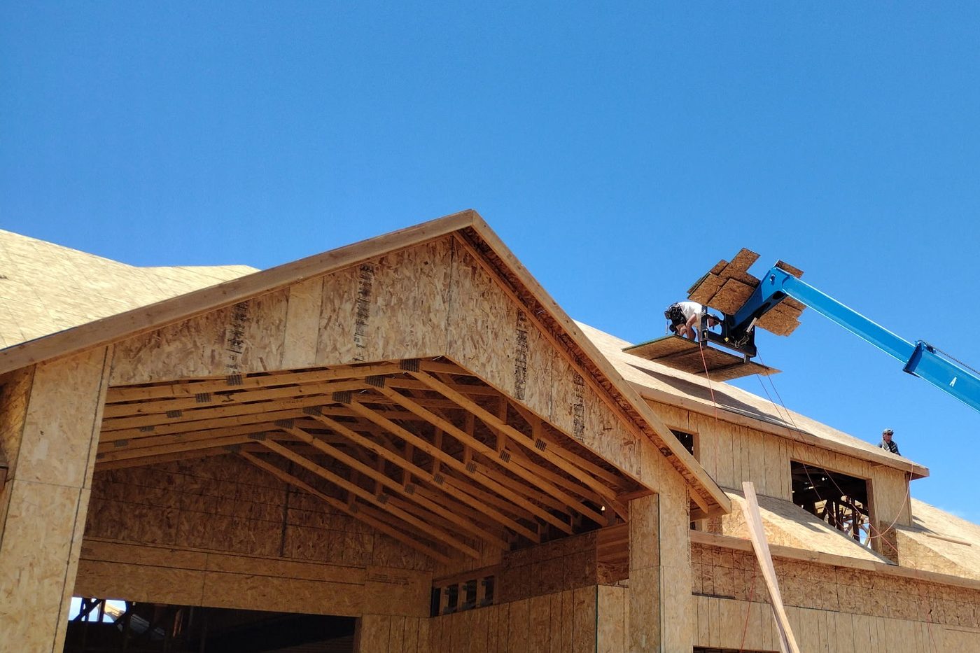 Crew lifting roof sheathing onto a framed home with a telehandler