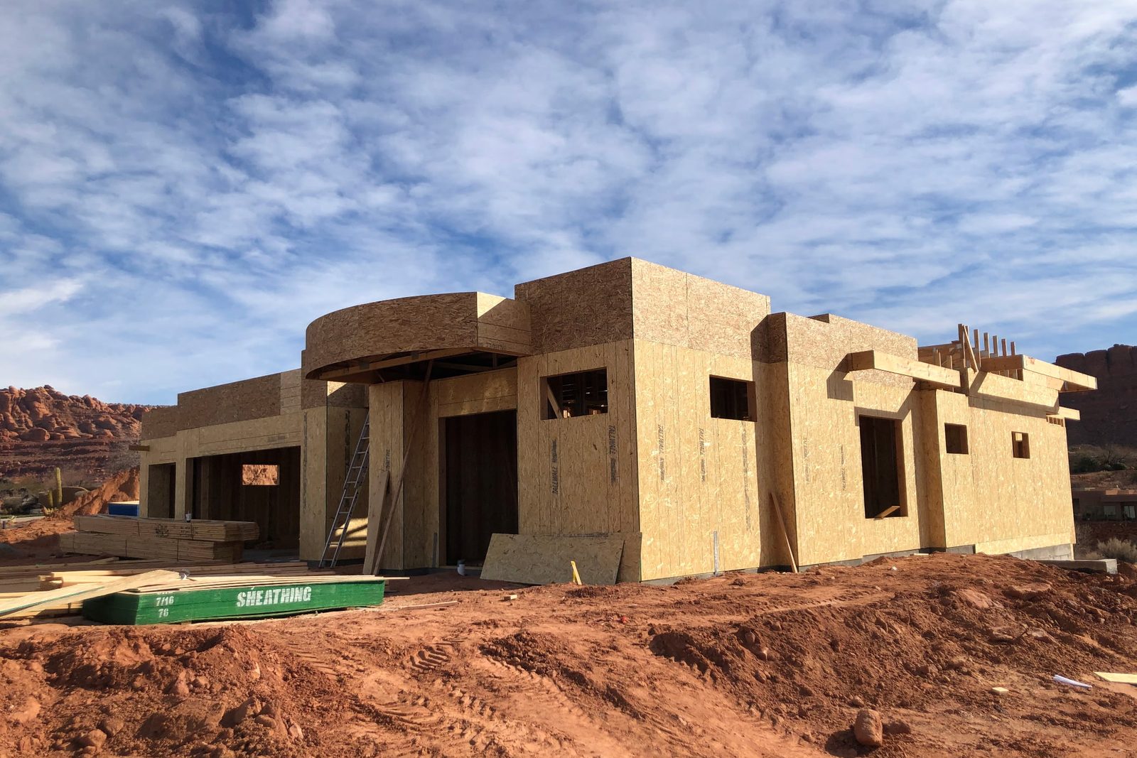 Sheathed wood-framed custom home under construction with red rock hills behind